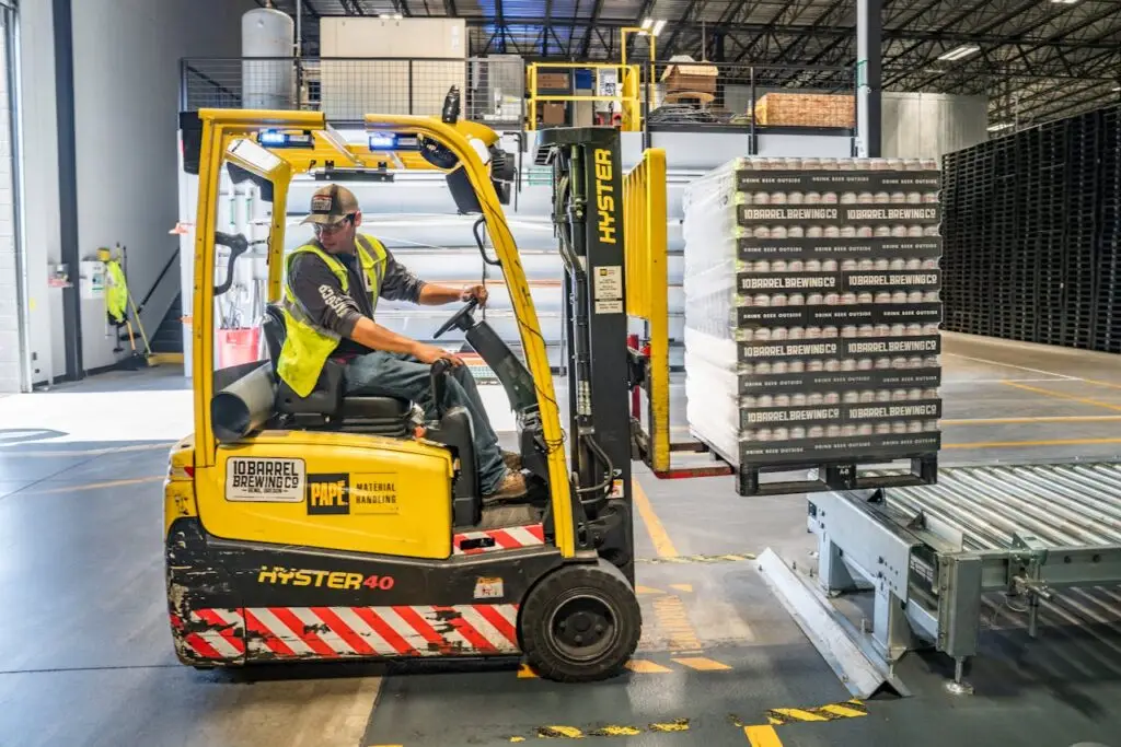 pexels photo 1267338 A warehouse worker maneuvers a forklift to transport crates for brewing company storage.